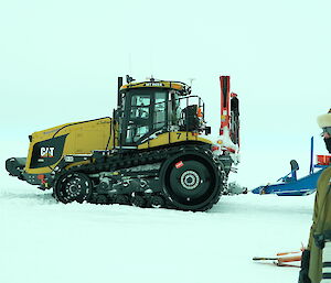 An expeditioner standing with a camera and a tractor behind