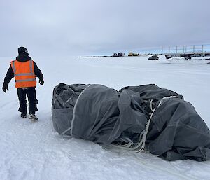 Expeditioner on the ground with a folded up parachute next to him on the ground