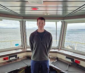 A man stands in front of ship's windows looking out over a river.