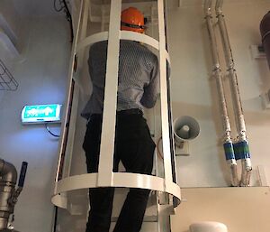 A man climbes up an emergency ladder, which has a cage around the outside.