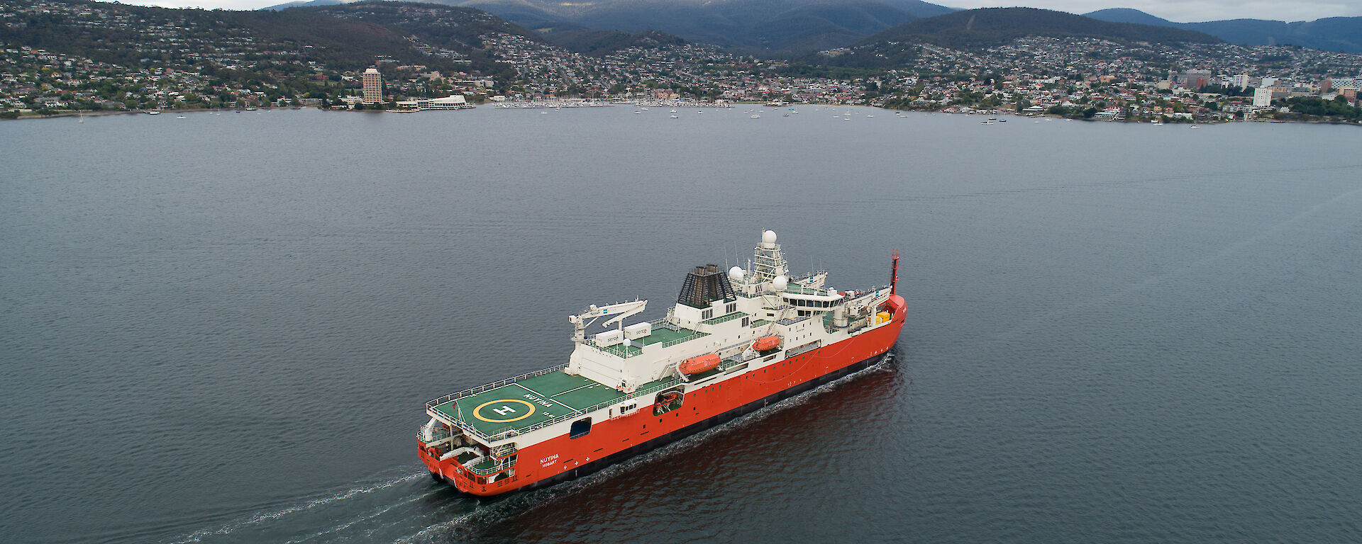A red and white ship sails up Hobart's Derwent River.