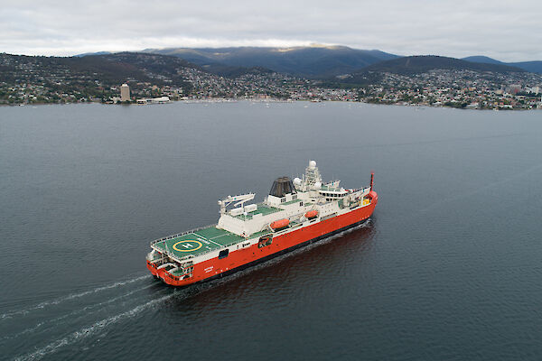 A red and white ship sails up Hobart's Derwent River.
