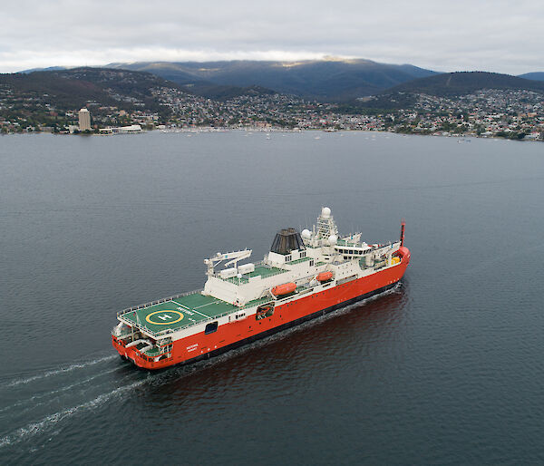 A red and white ship sails up Hobart's Derwent River.