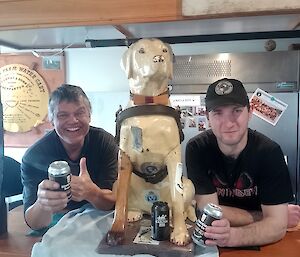 Stay, the Tasmanian Guide Dog's collection dog sits on a bar with a smiling man on each side of her
