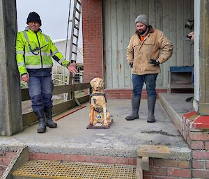 Two smiling men stand, one on either side, of a Guide Dogs Tasmania fibreglass collection dog.