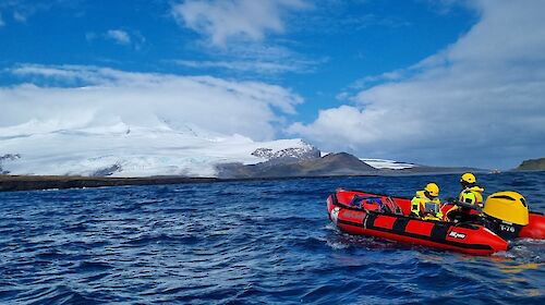 A red inflatable boat on the water in front of a snow-covered volcano