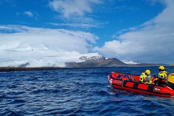 A red inflatable boat on the water in front of a snow-covered volcano