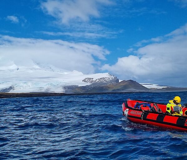A red inflatable boat on the water in front of a snow-covered volcano