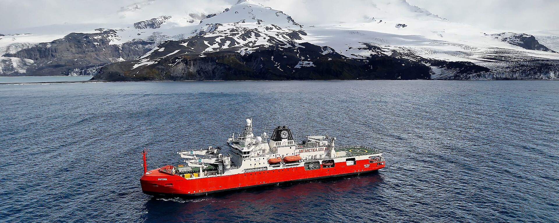Red and white icebreaker in front of snow covered mountain