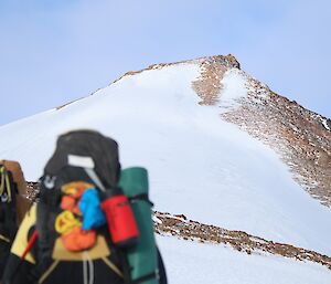 Photo of the summit of a mountain from behind a person with a large backpack on.