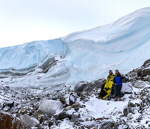 Three people standing in front of an ice cliff
