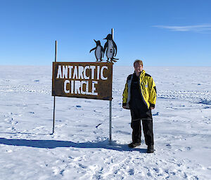 Man standing in front of sign saying Antarctic Circle