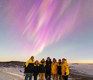 Seven people standing under an pink aurora-filled sky