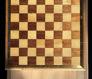 An overhead view of the completed chess board - squares of dark and light wood surrounded by brass inlays.