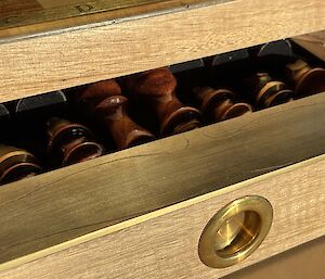 A partially opened drawer of a chess-set showing the dark wooden bases of several chess pieces.