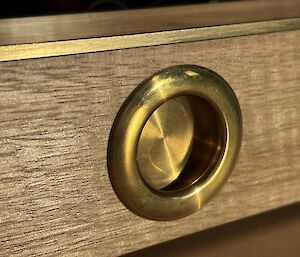 A round inset brass handle set into a wooden drawer face for opening the bottom drawer of the chess-set.