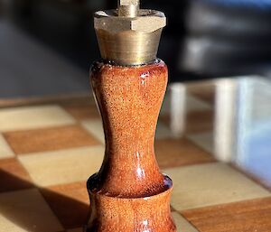 A close-up picture of the dark King piece sitting on the chess board. Made of Blackwood, it has a brass crown with a cross on top.