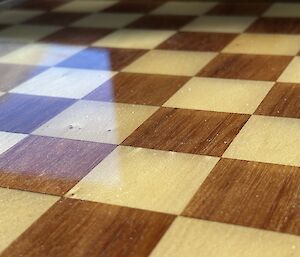 The sun reflects of the smooth surface of the light and dark squares of a chess board. The board is covered in a smooth epoxy resin.