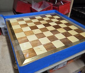 The almost completed chess board with blue painters tape around the edges to allow the application of epoxy resin to the wooden surface.