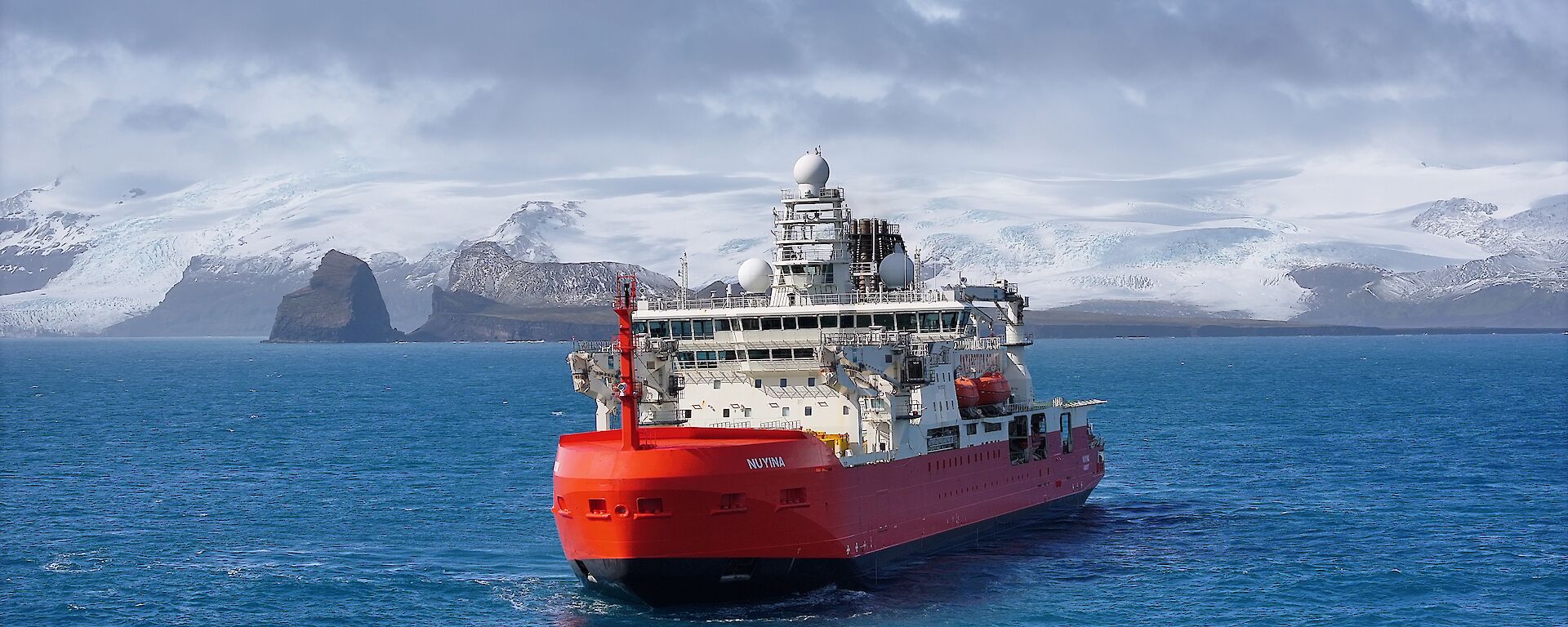 A red and white icebreaker in a bay with a snow-capped mountain behind it.