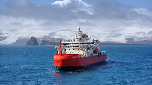 A red and white icebreaker in a bay with a snow-capped mountain behind it.