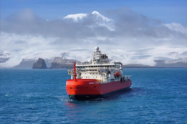 A red and white icebreaker in a bay with a snow-capped mountain behind it.
