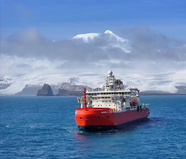 A red and white icebreaker in a bay with a snow-capped mountain behind it.