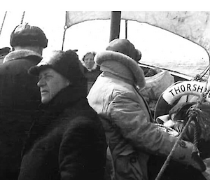 An old photo of about six people crowded together at the bow of a sailing ship with a life ring visible, with the words Thorshavn printed on it..