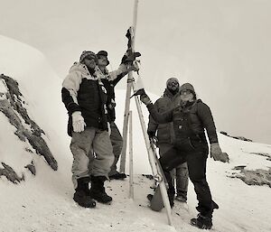 Four people standing around a flag pole aiming to recreate an old photo of people in a similar pose.
