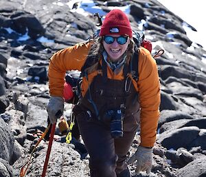 A woman with an ice axe and camera climbing a steep, rocky hill