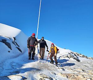 Three people standing at a tall pole marking the location of a cairn.
