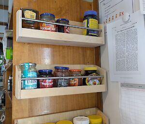 Three small shelves next to a toaster containing jars of various condiments for toast such as jams, honey, peanut butter and Vegemite