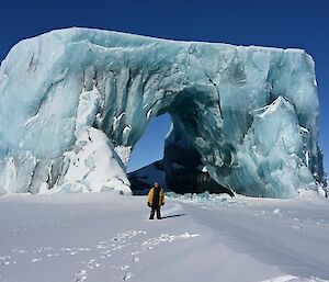 A person standing in front of an iceberg that is shaped like a marble arch