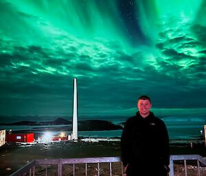 A man standing on a small metal porch with a green aurora overhead