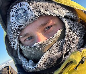 Close-up portrait of a person wearing an ice-covered beanie and balaclava