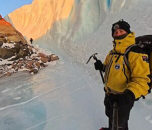 A person holding an ice axe stading at the base of an ice cliff