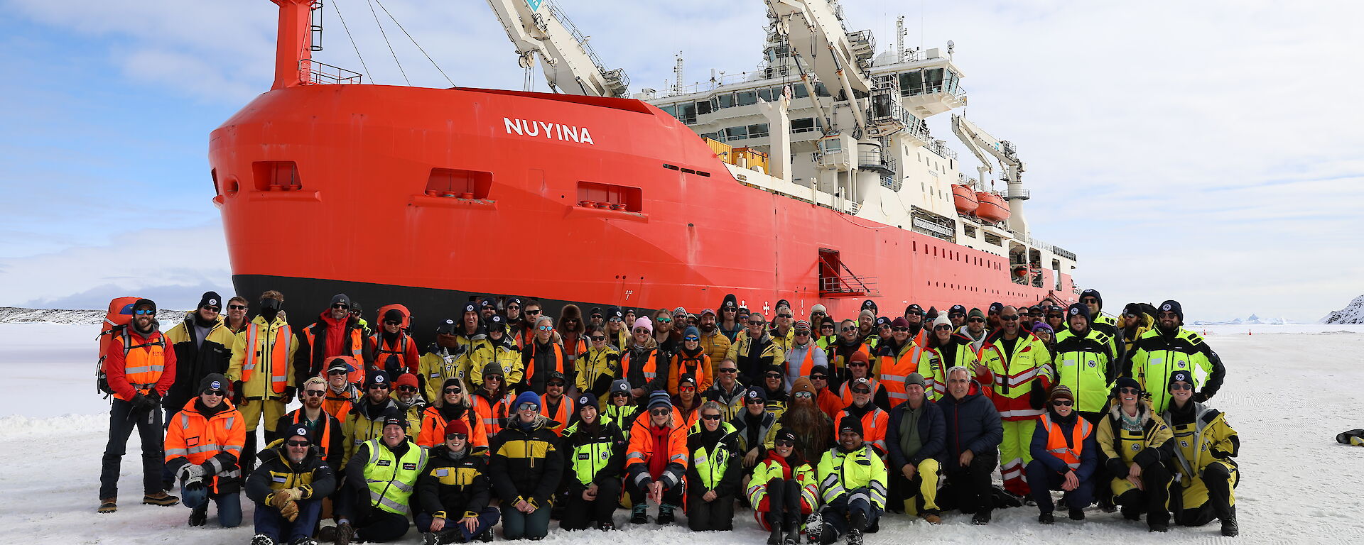 A group of people in outdoor gear on the ice in front of a red icebreaker ship
