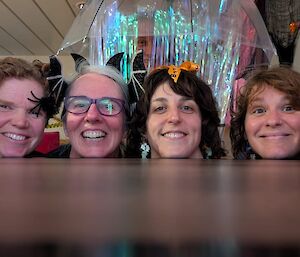 The heads of four smiling women, with skulls on either side