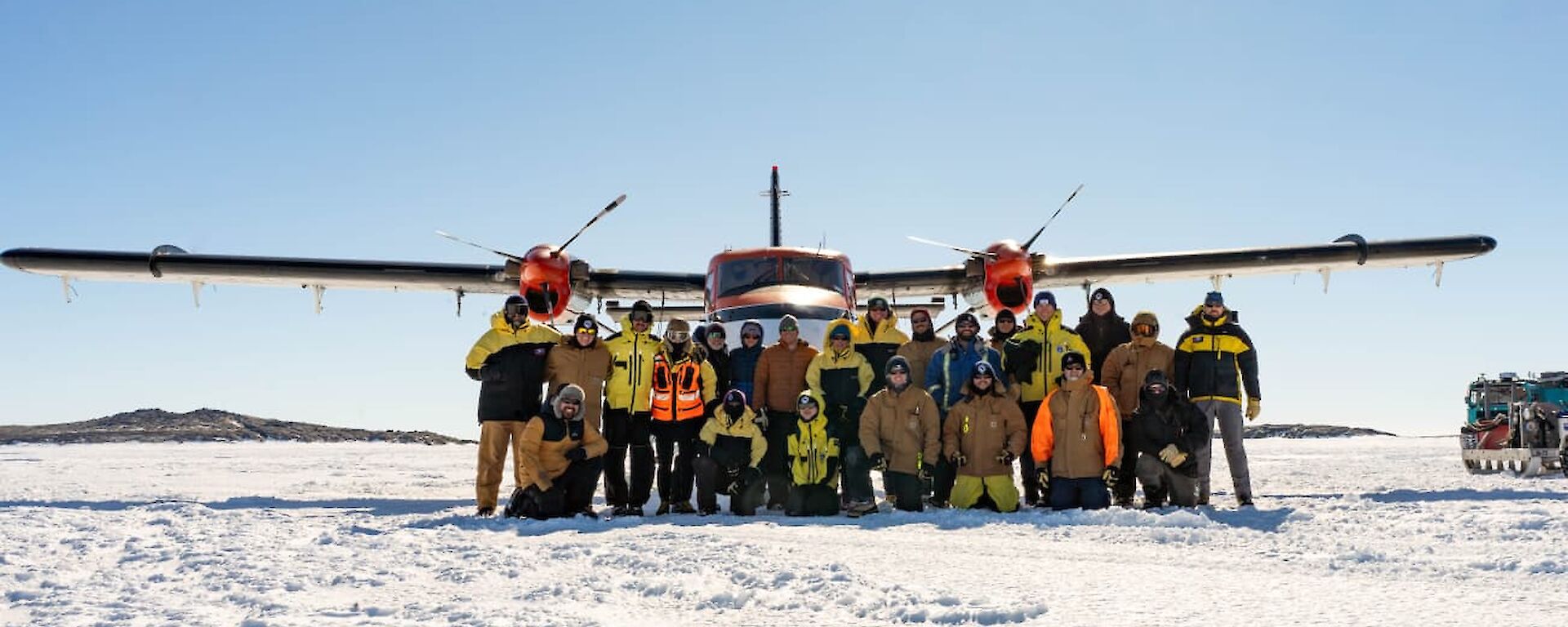 A group photo of Mawson expeditioners in front of a Twin Otter aircraft on the Mawson skiway