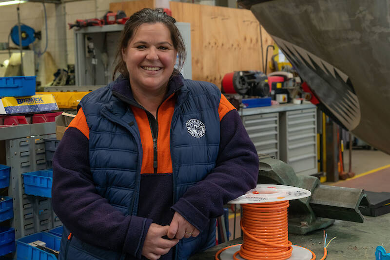 A woman standing beside a roll of electrical cable in a workshop.