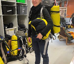 A woman stands wearing a field pack