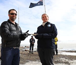 A man hands a large, ceremonial key over to a woman, standing beneath an Australian flag.