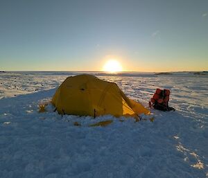 A yellow tent surrounded by snow