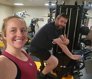 A man and a woman in exercise clothes riding stationery bikes in a gym area