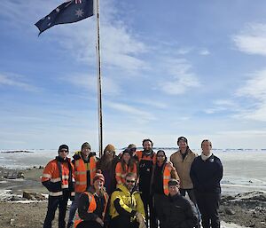 A group of 12 people gathered in front of a flagpole