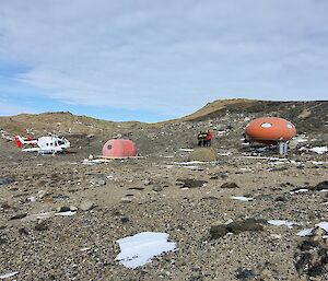 Two orange melon huts and a helicopter on a brown rocky surface