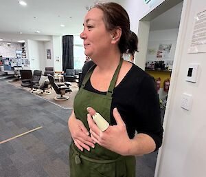 Brooke the chef stands (foreground) holding her left hand up to sow her finger bandage, with the lower lounge in the background