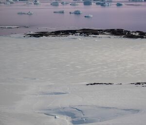 Image of icebergs in distance with snow covered terrain in foreground.