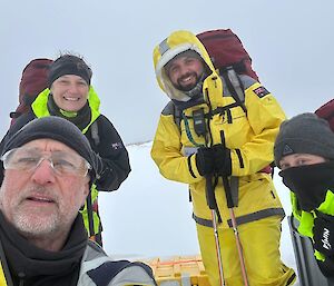 Four smiling people wearing outdoor clothing rugged up against the snow pose for a selfie.