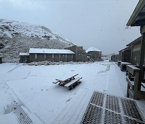 Snow covers the ground between buildings and the hill behind the buildings.